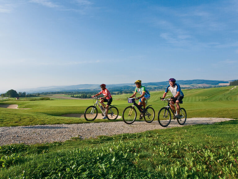 Eine entspannte Fahrradtour rund um Bad Birnbach auf einem Schotterweg mit Blick auf weite Felder und wolkigen Himmel.
