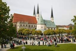 Eine Menschengruppe versammelt sich vor der eindrucksvollen Altöttinger Kirche, einem beliebten Wallfahrtsziel.